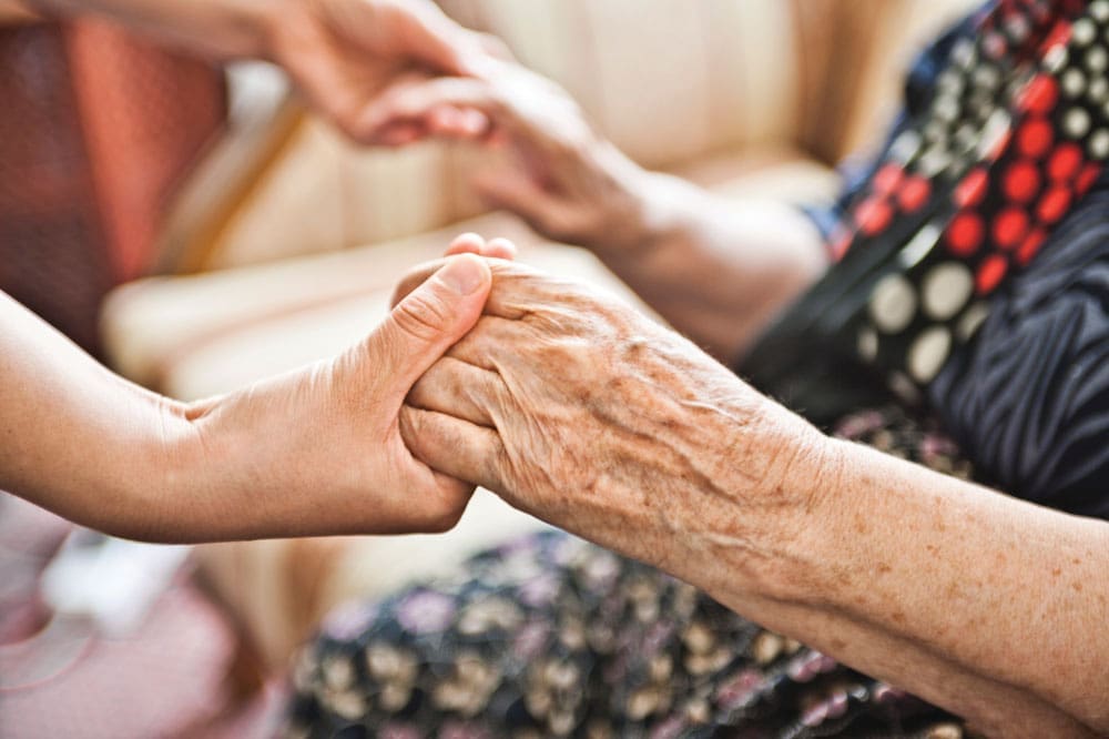 Senior living resident holding the hands of young adult
